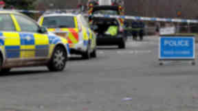 Road accident with police tape, two police cars and road closed sign in foreground.