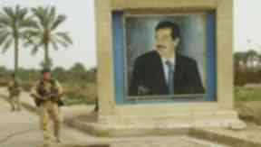 Coalition forces patrol beside Hussein mural.