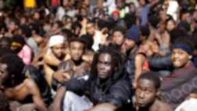 Migrants sit on the ground after storming a fence to enter Ceuta.