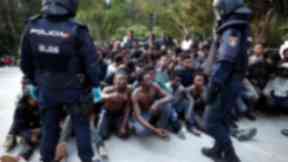 Migrants sit on the ground next to Spanish police officers after storming a fence to enter Ceuta.