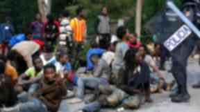 Migrants sit on the ground after storming a fence to enter the Spanish enclave of Ceuta.
