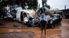 A barefoot man stands in front of a pile of vehicles after flash flooding near Athens.